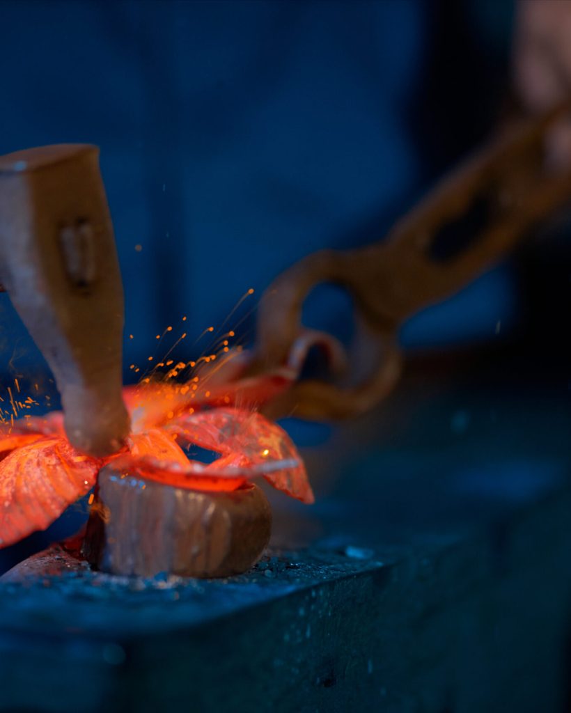 Close up senior man in dark blue suit working with special tools making decorations for fence in modern smithy. Concept of worker making decorations with fire in special place.